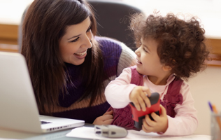 woman using a laptop computer with child playing nearby